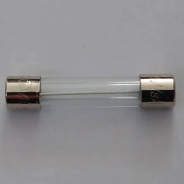 Glassäkring 1/8A med gyllene metalländar mot ljusgrå bakgrund, sedd rakt uppifrån i diagonal vinkel.